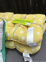 Four yellow and white polka dot cushions stacked, showing tufted design and labels indicating brand and size.