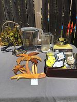 Overview of all items on outdoor table including pitchers, lamp base, wooden wall hanging, blender and flatware set packed in brown box