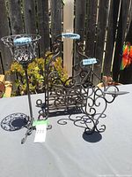 Photo showing all three metal holders on table outdoors with plants and fence background.