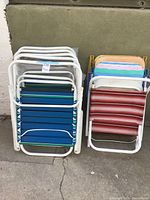 Stacked view of nine outdoor folding chairs with colorful plastic slats and white metal frames against a green wall.