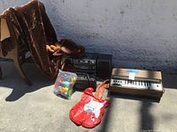 Wide view of all lot items including moose sleeping bag draped on chair, portable radio, boombox, toy container, and chord organ keyboard.