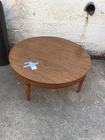 Full view of the round wooden coffee table on concrete ground showing tabletop and legs.