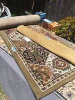 Photo showing the small decorative rug and the woven mat rolled on top of the runner rug, highlighting patterns and sizes.