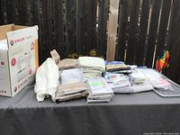 Singer Tradition 2250 sewing machine boxed with various curtain fabrics and packaged curtains displayed on outdoor table.