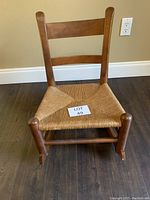 Front view of wooden child's rocking chair with woven wicker seat showing craftsmanship and condition.