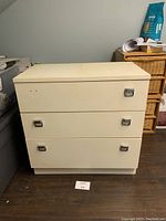 Front view of white 3-drawer dresser with metallic handles, showing damage and wear.