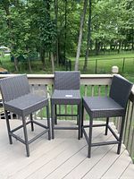 Three gray faux wicker bar stools shown together outside on a wooden deck with trees and a fence in background.
