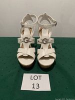 Front view of the white wedge sandals showing multiple straps and metallic 'G' buckle detail.