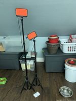 Two adjustable black tripods with rectangular orange diffuser LED lights mounted, set to different heights in an indoor room.