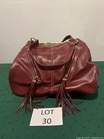 Front view of red handbag showing two vertical zippered pockets with leather fringe pulls and white stitching