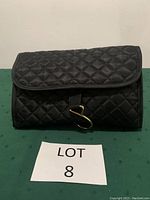 Closed black quilted toiletries bag with Velcro closure and gold-tone hook.