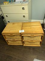 Photo of two wicker drawer units side by side, each with two wicker drawers and wooden frame, on a floor with a filing cabinet in the background.