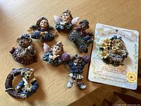 Overview of all eight Boyd's Bears collectible pins laid out on wooden surface, showing various characters including angels, bears on bases with inscriptions, and a floral collection pin on its original card.