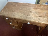 Top and side view of solid wood child's desk, showing surface wear and white drawer knobs.