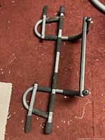 Chin-up bar disassembled and laid flat on carpet, showing metal frame and foam grips.