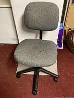Front view of the grey fabric office chair showing padded seat and backrest with black wheeled base.