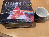 Pink Floyd metal lunch box with colorful prism and rainbow artwork and coffee mug showing part of the same design