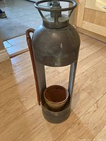 Full view of a vintage metal fire extinguisher body with a handle on top and slotted sides, housing a small terracotta pot inside as a planter.