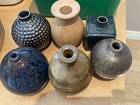 Photo of all six small pots arranged on a table with visible green bin in background, showing variety in shape and texture