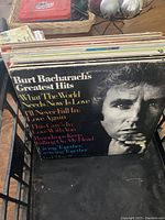 Side view of multiple vinyl LP records stacked in a basket, showing Burt Bacharach's Greatest Hits album on top with readable text and black-and-white portrait.