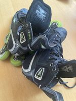 Pair of black Mission R80 Fuel inline roller skates with neon green wheels shown from an angled front view, highlighting the boot and lace details.