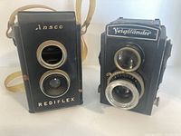 Front view of both vintage cameras showing their twin lens design and brand names Ansco Rediflex and Voigtlander Brilliant V6.
