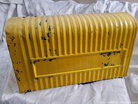 Front side view of the large yellow metal mailbox showing wear and black paint chipping