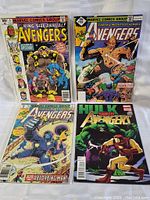 Top-down photo showing front covers of 4 Avengers comic books featuring several characters including Absorbing Man, Arsenal, Monolith, Hulk, and Iron Man.