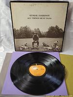 Vinyl record with orange label visible on purple paper sleeve, in front of the album cover.