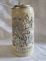 Side view of the large lidded beer stein showing detailed relief of Oktoberfest scene with ferris wheel, horses, and carriage.