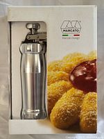 Photo of the Marcato branded metal cookie press in its original packaging with visible plunger handle and body