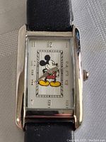 Close-up front view of the Mickey Mouse themed rectangular watch face with silver-tone frame and black strap.