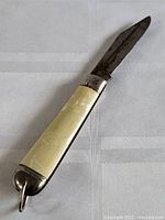 Vintage folding pocket knife partially opened showing the metal blade and cream-colored handle with silver metal caps and a keyring loop.