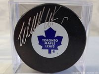 Top view of the black hockey puck showing the Toronto Maple Leafs logo and silver autograph by Wendel Clark, inside a clear display case.