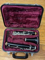 Clarinet disassembled inside hardshell case showing upper joint, lower joint, bell, and barrel in velvet compartments