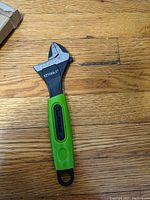 Photo of a new EZ Tools variable adjustable wrench with a green handle lying on a wooden surface.