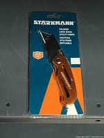 Photo of a new Starkmann folding lock-back utility knife in original blister packaging, showing the knife handle and blade covered by plastic sheath with box graphics.