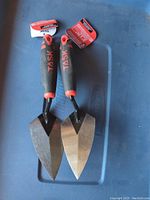 Pair of new TASK pointing trowels with black and red Flex Fit handles and triangular steel blades on a blue surface.