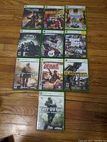Photo of all 10 Xbox 360 game cases arranged on wooden floor showing cover art: Gears of War, Borderlands, Saints Row 2, Fallout 3, Splinter Cell, GTA Liberty City, Call of Duty Modern Warfare 2, Rainbow Six Vegas 2, Operation Flashpoint Dragon Rising, Call of Duty 4