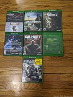 Top-down photo of all seven Xbox One game discs laid out on a wooden floor showing front covers and game titles.