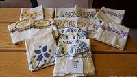 Overview of 7 sets of embroidered pillowcases laid on table showing varied floral embroidery and 'His' and 'Hers' labeled pillowcases.