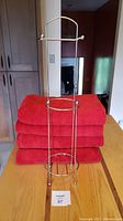Four large red cotton towels stacked together with chrome toilet paper holder standing upright in front.