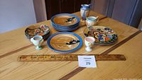 Overview of six plates, four saucers, two eggcups arranged on wooden table with ruler for scale.