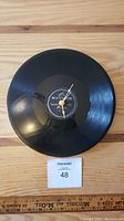 Full view of the black vinyl LP record clock seen from the front on a wooden surface with measurement ruler below.