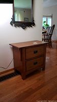 Side view of the two drawer wooden Mission-style side table against a wall with hardwood floor.