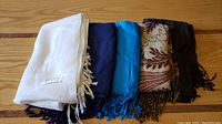 Five scarves laid out side by side showing different colors and patterns including solid, patterned, and labeled scarf.