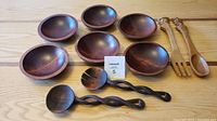 Photo showing six round wooden salad bowls arranged with four carved wooden salad servers on a wooden surface.