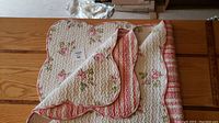 Quilt folded to show both floral and striped sides, placed on wooden tabletop.