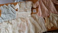 Full view of all vintage baby clothes displayed together showing various dresses, a pink silk coat, and knit socks.