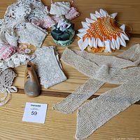Top view of assorted crochet and lace trims, wooden shoe last, and decorative pincushions on wood surface.